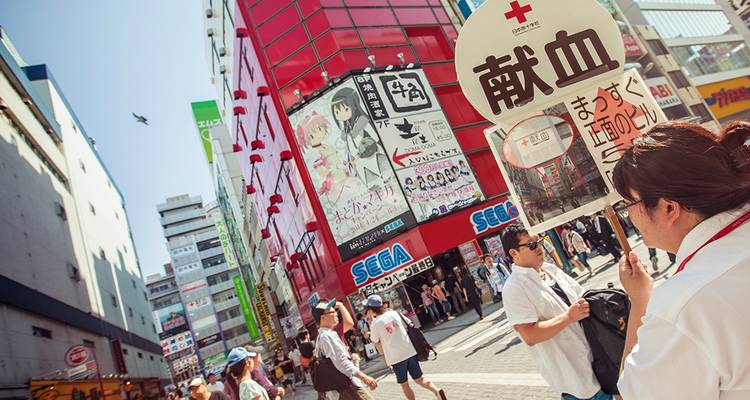 Calle concurrida de Akihabara con carteles de anime coloridos y peatones bajo un cielo brillante