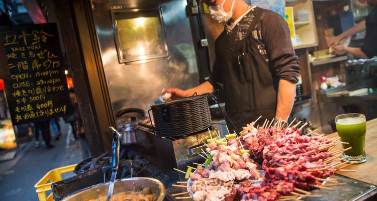 Vendedor callejero asando brochetas yakitori variadas en un puesto de mercado nocturno