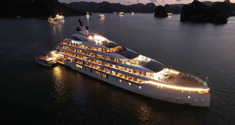 Yacht illuminé naviguant la nuit avec un paysage pittoresque en arrière-plan.