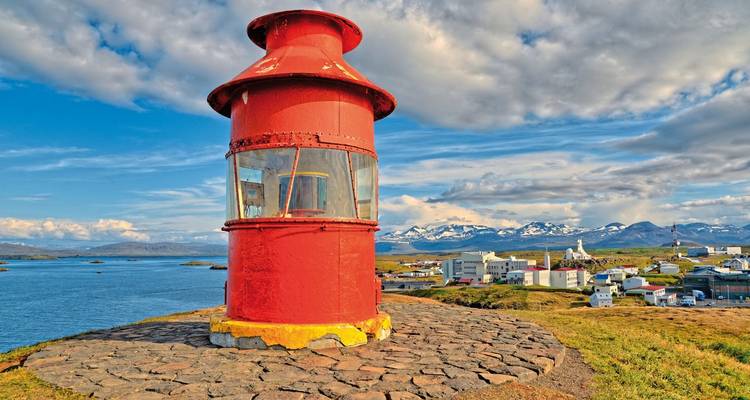 Roter Leuchtturm mit Blick auf eine Küstenstadt mit schneebedeckten Bergen.