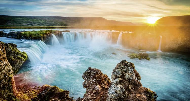 Lebendiger Wasserfall mit einem Regenbogen in einer grünen Schlucht bei Sonnenuntergang.