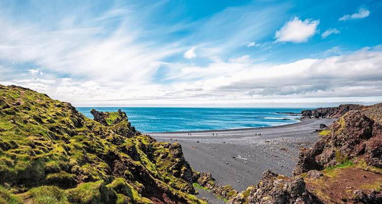 Felsige Küste mit einem schwarzen Sandstrand und Meerblick an einem sonnigen Tag.