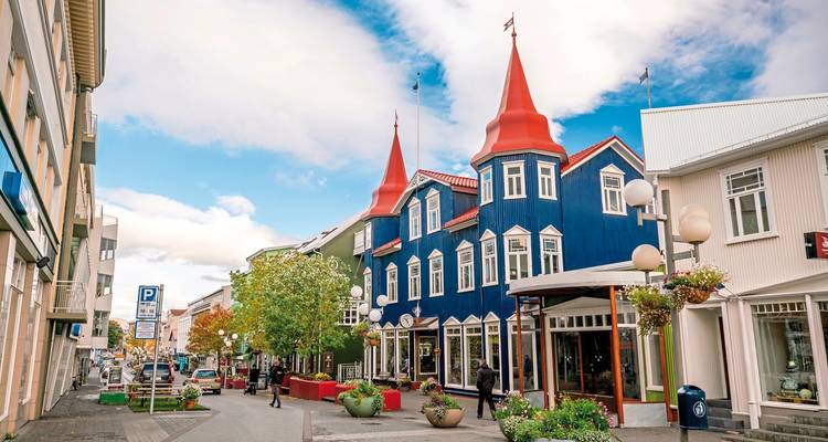Buntes Gebäude mit roten Dächern an einer Straße mit Menschen in einer Stadt.