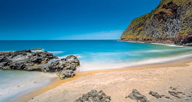 Idyllischer Strand mit kristallklarem blauen Meer und felsiger Küste.