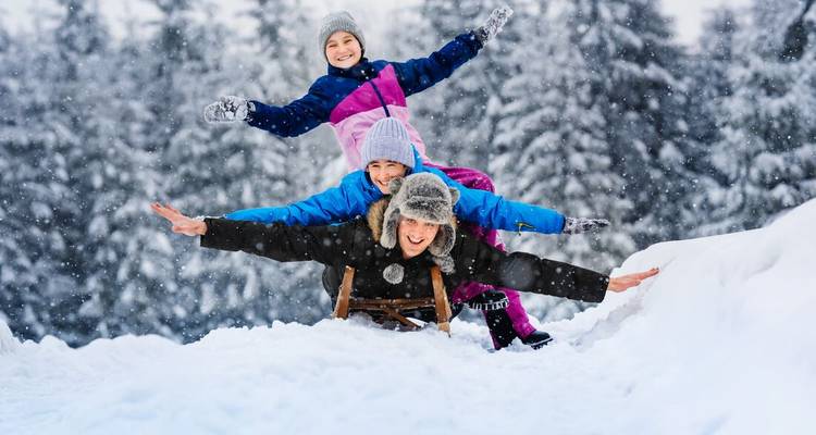 Trois personnes profitant de la luge dans des conditions neigeuses.
