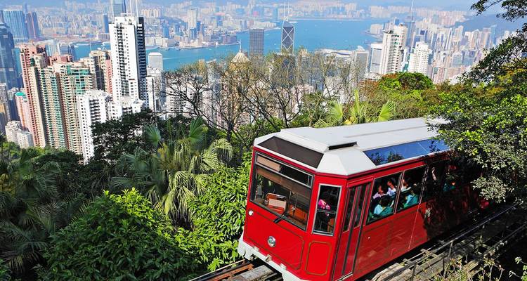 Iconic red Peak Tram climbing through lush greenery with Hong Kong skyline and harbor below