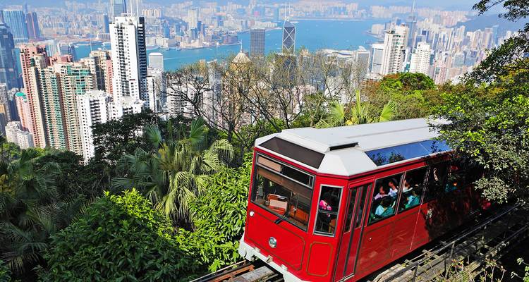 A red tram climbing up a hill with a view of the cityscape and a harbor.