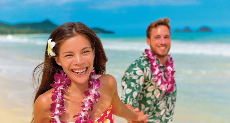 Happy couple on a beach with lei garlands.
