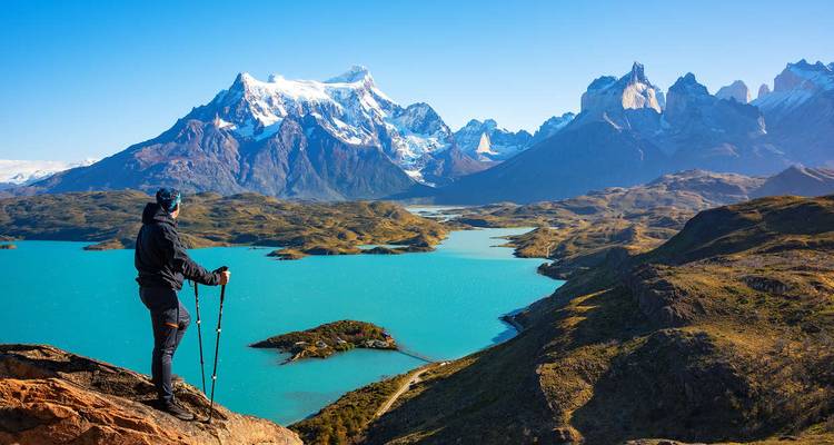 Hiker overlooking a turquoise lake and mountain range.
