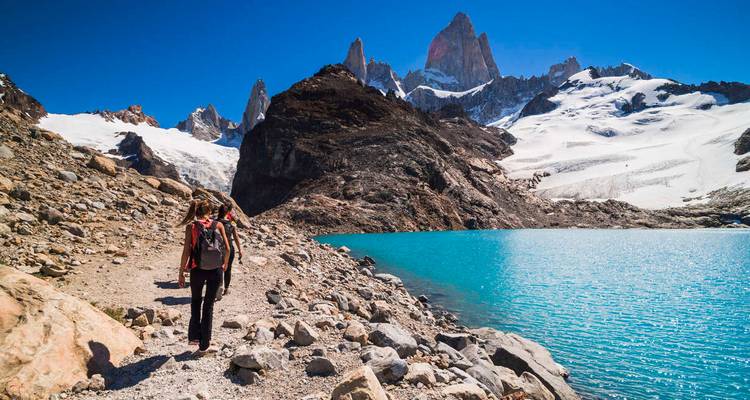 Hiker walking by a turquoise lagoon and mountain.