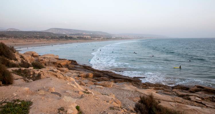 Une large plage avec des surfeurs au loin sous un ciel couvert.