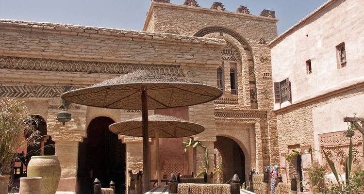 Patio de una kasbah histórica con sombrillas tejidas, muros de piedra y patrones decorativos.