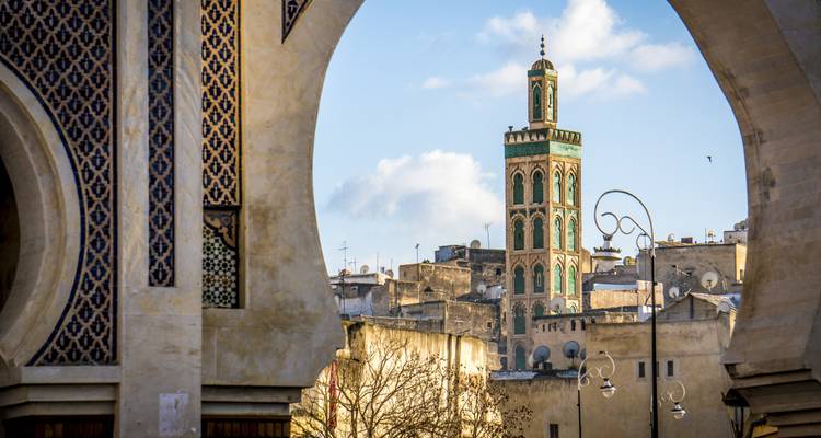 Vue d'une ville à travers des arcades ornementées avec une tour proéminente.