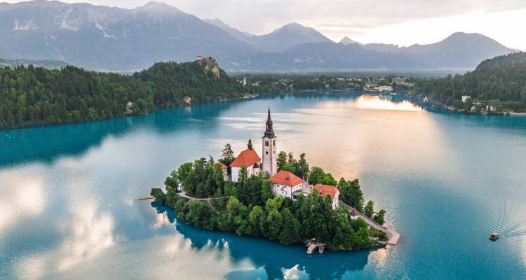 Vue aérienne au lever du soleil du lac de Bled avec l'église Sainte-Marie sur sa petite île et les Alpes juliennes en arrière-plan.
