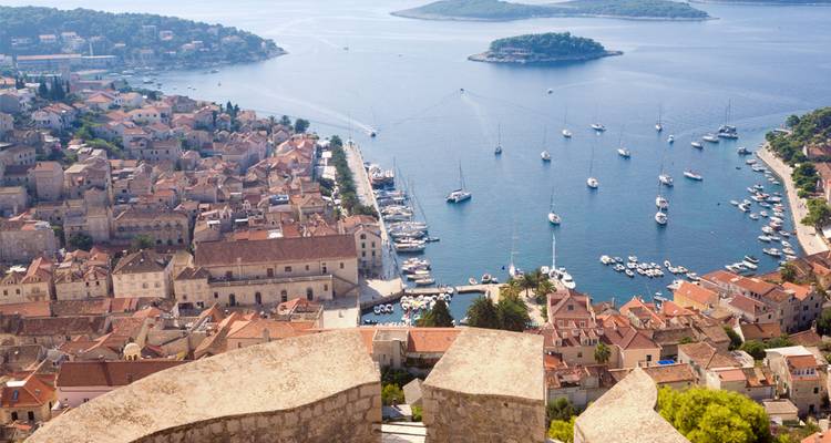 Vista panorámica de un pueblo costero con techos de terracota, una marina llena de yates e islas diminutas en el mar.