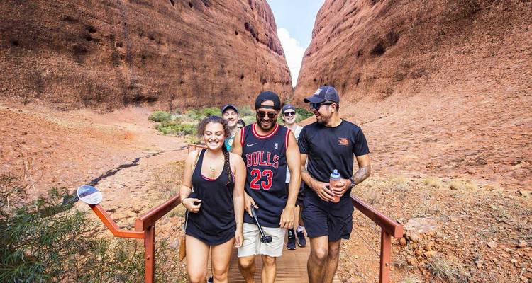 Group of people hiking between large rock formations in a desert landscape.