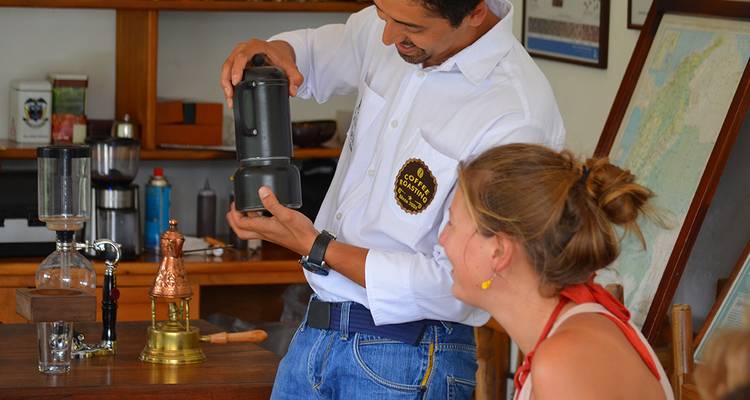 Un guide souriant montrant un processus de préparation du café à un visiteur.