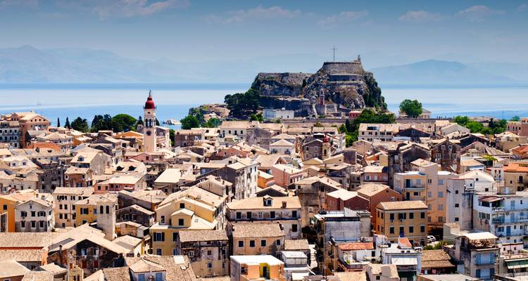 Vista aérea de los tejados ocres de la Ciudad de Corfú dominados por la Fortaleza Antigua y el campanario, con el Mar Jónico brillando más allá.