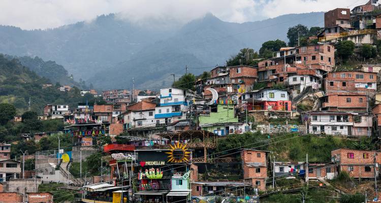 Barrio colorido en la ladera de Medellín con montañas envueltas en nubes al fondo.