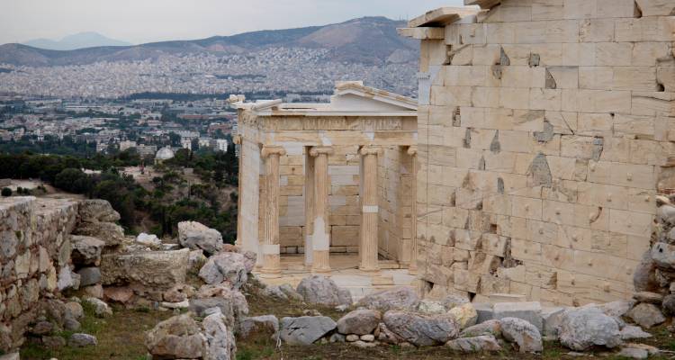 Anciennes ruines de pierre avec une ville en arrière-plan, sous un ciel nuageux.
