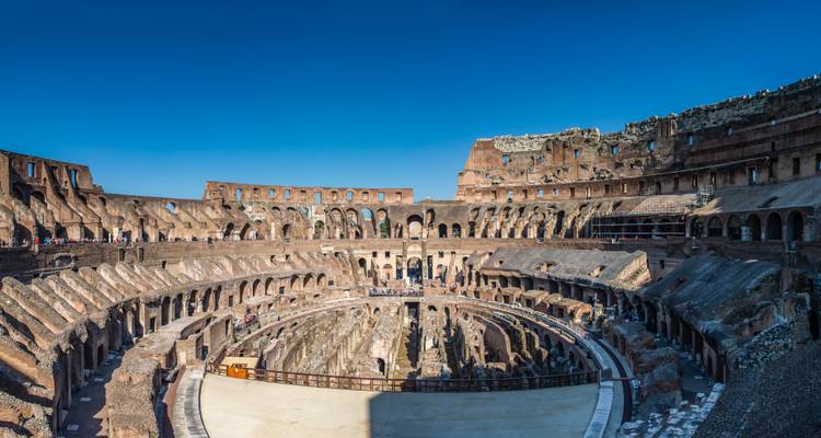 Panorama de l'arène intérieure et des gradins du Colosseum de Rome sous un ciel bleu dégagé.