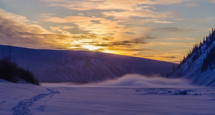 Lever de soleil matinal sur une vallée enneigée avec de la brume.
