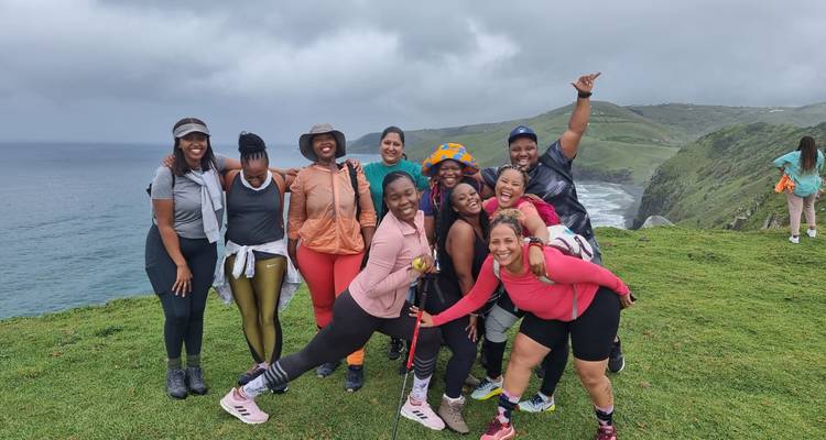 Un groupe de randonneurs joyeux pose sur un promontoire herbeux surplombant des falaises spectaculaires et les vagues en contrebas par temps gris.