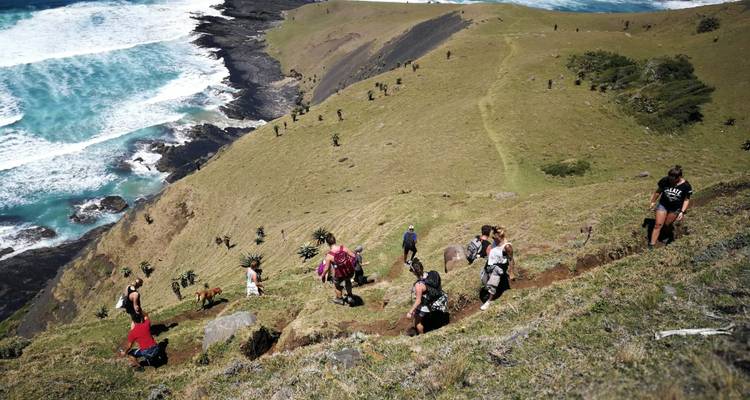 Les randonneurs grimpent sur une crête herbeuse escarpée dominant les vagues turquoise qui se brisent contre la roche noire.