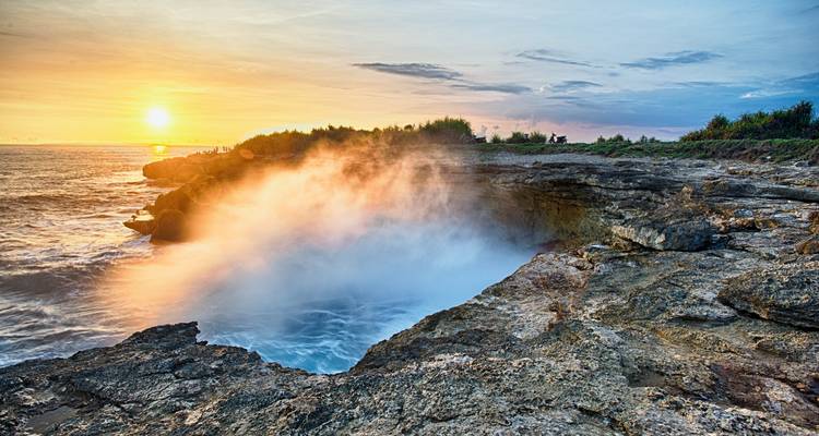 Sonnenlicht beleuchtet die Gischt, die aus einem Blasloch in den zerklüfteten Küstenfelsen von Nusa Lembongan aufsteigt.