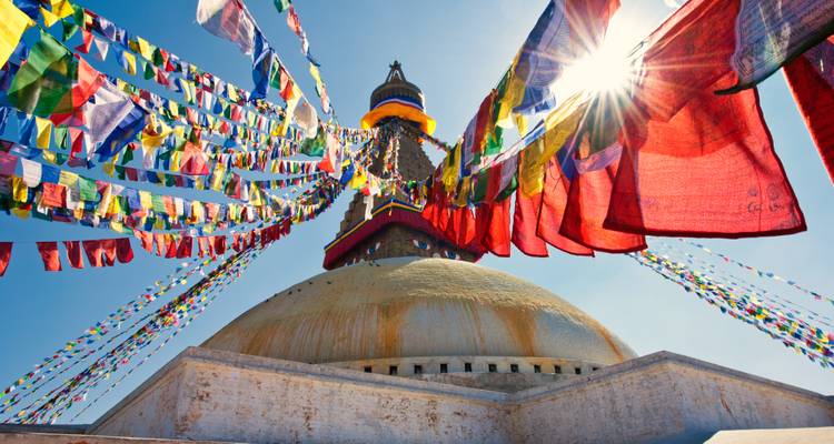 Des drapeaux de prière flottent depuis le stupa blanc de Boudhanath tandis que le soleil flamboie derrière sa flèche.
