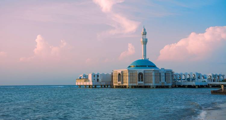 Weiße schwimmende Moschee mit türkisfarbener Kuppel, die sich über das Rote Meer bei pastellfarbenem Sonnenuntergang erstreckt.