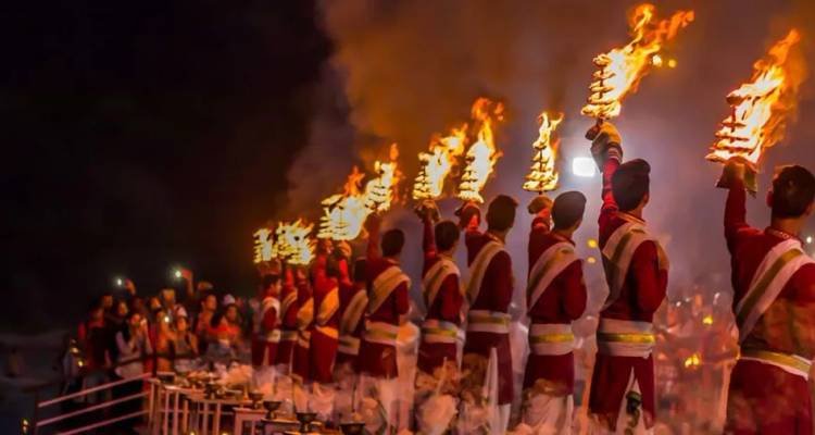 Evening Ganga Aarti style ceremony with rows of priests waving flaming lamps before a crowd.