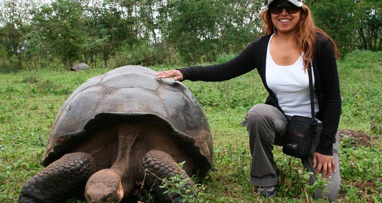 Un viajero sonriente se arrodilla junto a una tortuga gigante en exuberante pastizal de las tierras altas.
