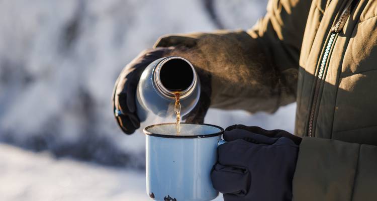 Gros plan d'une personne versant une boisson chaude dans une tasse à l'extérieur dans un décor enneigé.