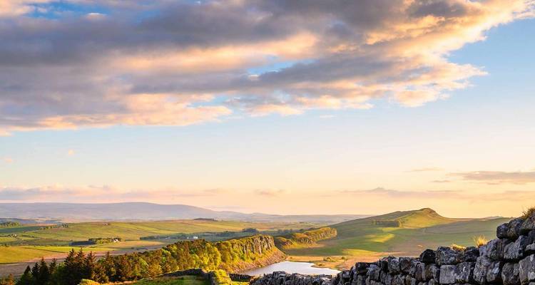Hadrianusmuur slingert door glooiend groen landschap onder een dramatische avondhemel