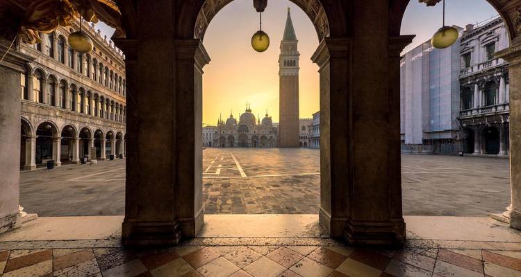 Vue du lever du soleil sur la place Saint-Marc encadrée par la colonnade voûtée, avec le Campanile et la Basilique à Venise.
