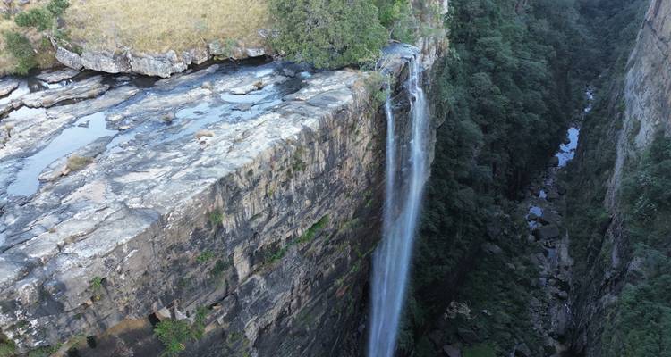 Drone view of a tall waterfall plunging into a deep forested gorge.