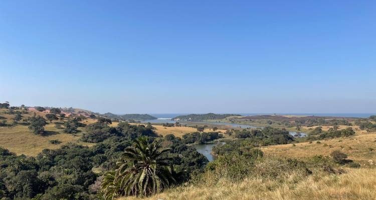 Expansive view of rolling grasslands, river and distant sea under a clear blue sky.