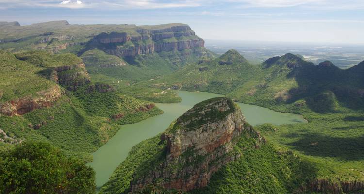 Weids luchtfoto van een groene kloof met kronkelende rivier en dramatische rotswanden.