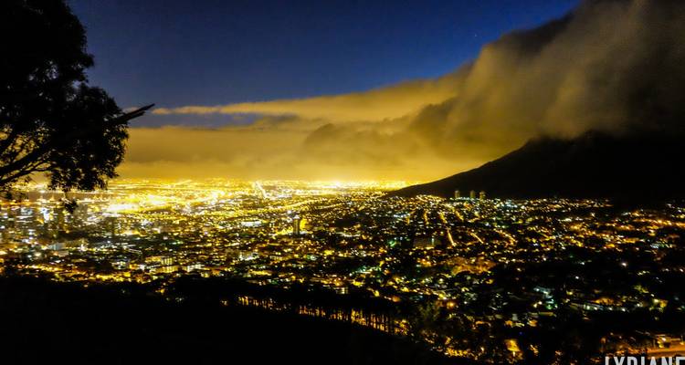 Een glinsterende stadslandschap strekt zich uit onder een berg in de nacht, met wolken die gloeien van het stadslicht.
