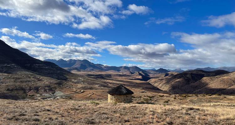 Breed bergdal landschap met een enkele kleine ronde stenen hut onder een blauwe hemel met verspreide wolken.