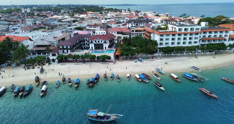 Luchtfoto van de waterkant van Stone Town met boten voor anker in turquoise water en historische gebouwen langs het strand.