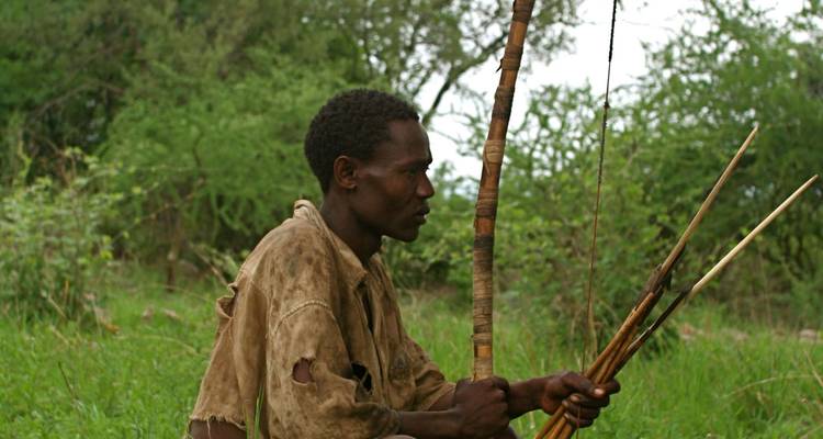 Mann sitzt mit Pfeilen in einem grasbewachsenen Bereich.