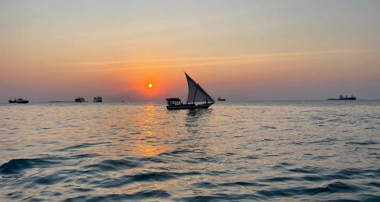Silhouet van een traditionele dhow die bij zonsondergang over kalme oceaanwateren vaart.