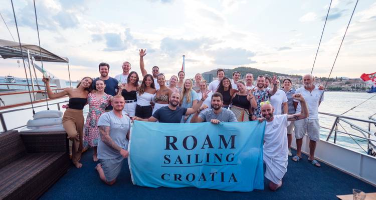 Gruppe von Menschen, die ein Roam Sailing Banner auf einem Boot halten.