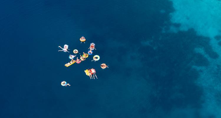 Menschen, die mit Schwimmhilfen in kreisförmiger Anordnung auf dem Wasser treiben.