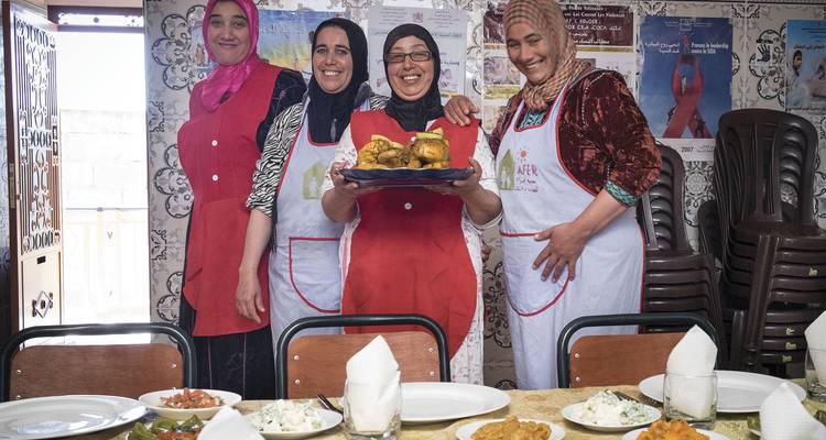 Les femmes locales en tabliers présentant fièrement les plats traditionnels à l'intérieur d'une cuisine communautaire.