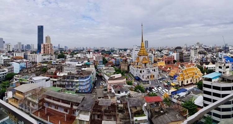 Panorama urbain avec un temple aux toits dorés s'élevant parmi les immeubles modernes densément construits sous un ciel nuageux.