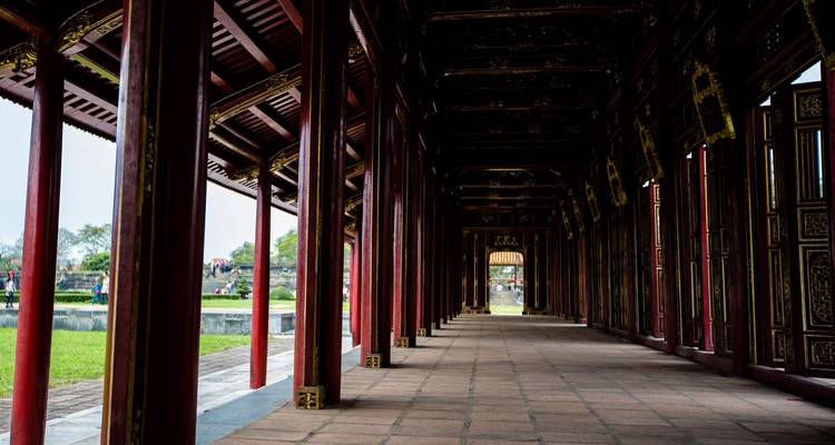 Long couloir couvert bordé de colonnes en bois rouge menant vers les jardins historiques de la Cité Impériale de Huế.