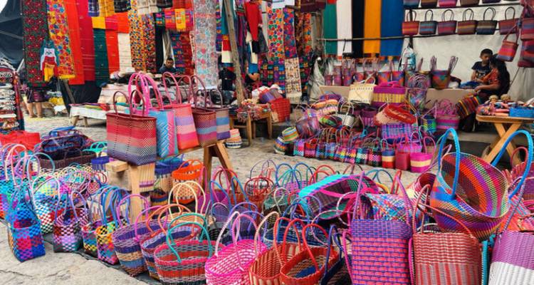 Scène de marché animée avec des sacs colorés and des textiles en exposition.